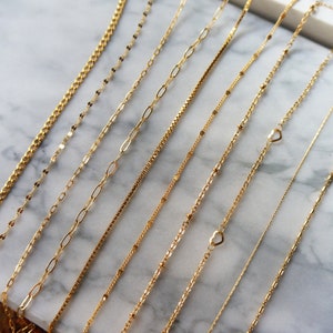 May include: A collection of delicate gold necklaces displayed on a marble surface. The necklaces feature various chain styles, including box, paperclip, and beaded designs. Some necklaces have heart-shaped pendants.