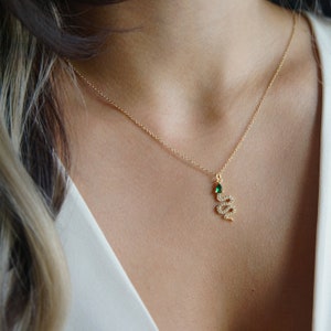 May include: A gold chain necklace with a small snake pendant. The snake is adorned with small clear stones and has a single green stone for an eye.