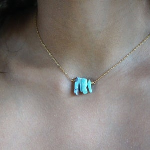 May include: A gold chain necklace with a pendant made of several small, turquoise-colored stones.