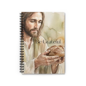 Pode incluir: Caderno espiral com uma ilustração em aquarela de uma figura religiosa segurando pão. A imagem tem uma paleta de cores quentes e o texto "Be Grateful" em uma fonte simples.