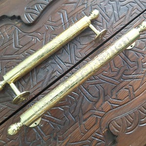 Könnte beinhalten: Zwei verzierte goldene Türklinken mit komplizierten Designs. Die Griffe sind aus Metall und haben eine polierte Oberfläche.