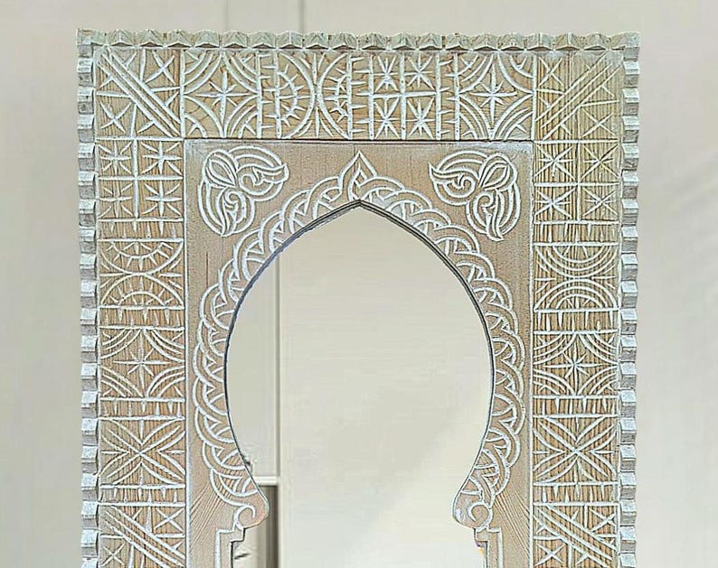 May include: A white wooden mirror with an ornate carved frame. The frame features a geometric pattern with a central arch.
