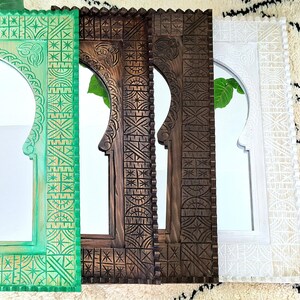 May include: Three wooden mirrors with intricate carved designs. The mirrors are in different colors: green, brown, and white. Each mirror has an arched top and a rectangular frame.