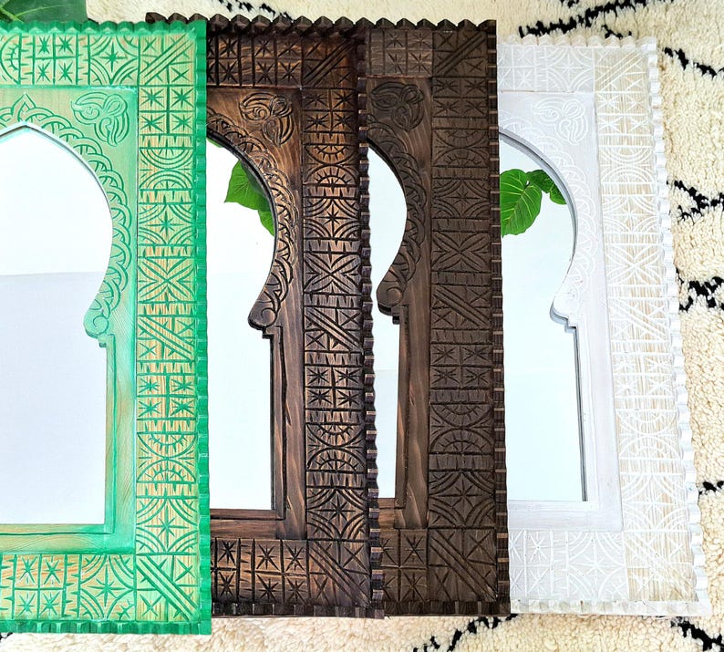 May include: Three wooden mirrors with intricate carved designs. The mirrors are in different colors: green, brown, and white. Each mirror has an arched top and a rectangular frame.
