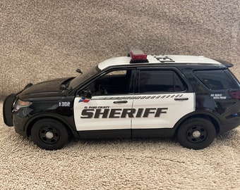 May include: A black and white El Paso County Sheriff's Department Ford Explorer police car with the words "We Serve With Pride" on the back. The car has a red light on top and the number 1302 on the side.