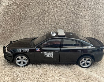 Puede incluir: Modelo de coche de juguete negro de un Dodge Charger de la Patrulla de Carreteras de Oklahoma. El coche tiene una etiqueta blanca "STATE TROOPER" en el lateral y un "401" en el techo. El coche tiene una etiqueta blanca "OKLAHOMA HIGHWAY PATROL" en el lateral.