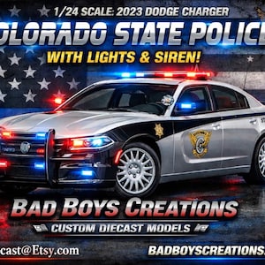 May include: A 1/24 scale model of a 2023 Dodge Charger Colorado State Police car with lights and siren. The silver and black vehicle features emergency lights and the text "Colorado State Police" and "Bad Boys Creations". The background shows an American flag.