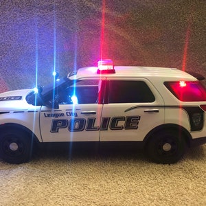 May include: White police car with blue and red flashing lights. The car has "League City POLICE" written on the side.