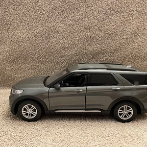 May include: A grey SUV model with black trim and silver wheels. The vehicle has tinted windows and a roof rack. The model is a detailed replica of a modern SUV.