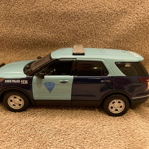 May include: A blue and black toy police car with a white roof and a white "STATE POLICE" emblem on the side. The car has a white number "1536" on the side.