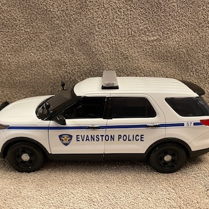 May include: White police car with blue and silver accents. The car has "EVANSTON POLICE" written on the side and the number "57" on the back.
