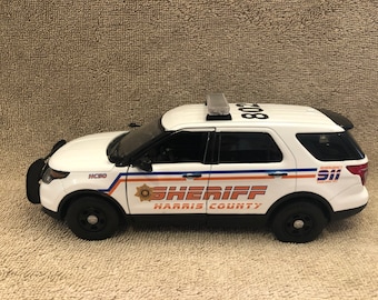 Puede incluir: Un todoterreno de policía de juguete blanco y negro con las palabras "SHERIFF HARRIS COUNTY" y "911 EMERGENCY" impresas en el lateral. El vehículo tiene una barra de luces en la parte superior y ruedas negras.