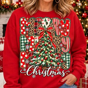 May include: A red long-sleeve sweatshirt featuring a large graphic print of a Christmas tree decorated with red ornaments and lights. The text MERRY MERRY MERRY is displayed in a patchwork style with various patterns, and the word Christmas is below.