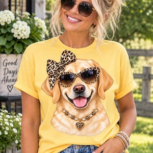 May include: A bright yellow short-sleeve t-shirt featuring a graphic print of a golden retriever dog. The dog is wearing leopard print sunglasses, a matching leopard print bow on its head, and a gold-toned necklace with a heart-shaped pendant.
