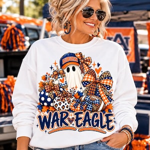 May include: A white long-sleeve sweatshirt featuring a graphic print of a ghost wearing an Auburn baseball cap, surrounded by pumpkins, a football, and large bows in orange, blue, and white. The text WAR EAGLE is printed in blue and orange.