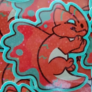 May include: A collection of stickers featuring a cartoon squirrel in shades of red and orange. The squirrel is outlined in black and has a teal border. The background has a glittery effect with stars and teal accents.