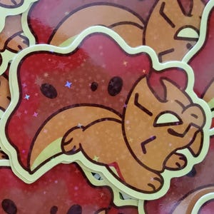 May include: A collection of stickers featuring a cartoon lion in red and orange. The stickers have a holographic effect and a yellow border. The lion is depicted in a relaxed pose.