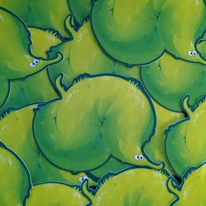 May include: A close-up of a pile of green and yellow cartoon stickers. The stickers are shaped like a creature with large eyes and a long, thin body.