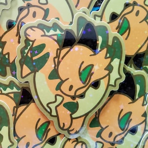 May include: Holographic stickers with a cartoon dragon design in orange, green, and yellow. The dragon has a friendly face and is outlined in gold. The stickers have a shimmering, iridescent effect, with a gold border.