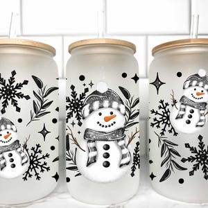 May include: Three frosted glass tumblers with bamboo lids and straws. Each tumbler features a black and white snowman design with snowflakes and black dots.