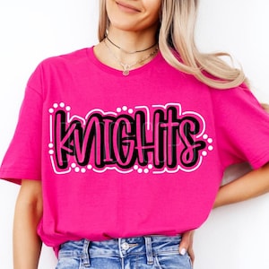 May include: A pink t-shirt with the word "Knights" written in black and white lettering.
