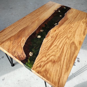 Pode incluir: Uma mesa de centro de madeira com uma incrusta&ccedil;&atilde;o de rio de resina ep&oacute;xi verde escura e preta. A incrusta&ccedil;&atilde;o apresenta acentos brancos salpicados. A mesa tem pernas de cabelo preto.