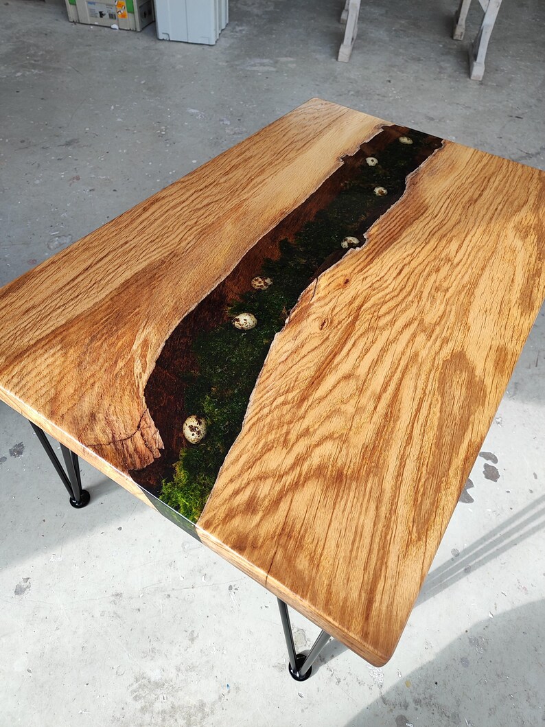 Pode incluir: Uma mesa de centro de madeira com uma incrusta&ccedil;&atilde;o de rio de resina ep&oacute;xi verde escura e preta. A incrusta&ccedil;&atilde;o apresenta acentos brancos salpicados. A mesa tem pernas de cabelo preto.