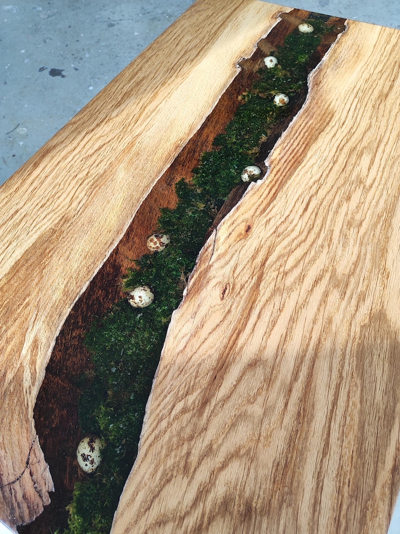 Pode incluir: Uma mesa de madeira com acabamento de gr&atilde;o de madeira natural. Uma rachadura na madeira &eacute; preenchida com resina transparente e musgo. Ovos brancos salpicados est&atilde;o embutidos na resina.