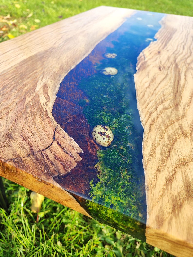 Pode incluir: Uma mesa de madeira com um rio de resina azul claro correndo pelo centro. A resina cont&eacute;m musgo e ovos de codorniz. A mesa &eacute; feita de madeira natural com um acabamento r&uacute;stico.
