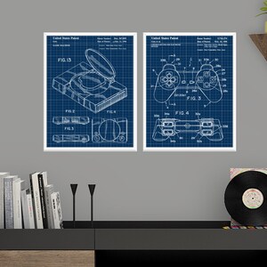 May include: Two framed prints featuring blueprint-style illustrations of a gaming console and controller. The prints show detailed technical drawings in white against a blue grid background, ideal for a games room.
