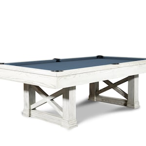 May include: A white pool table with a blue felt top and a farmhouse style base. The table has a wooden frame and legs with a distressed white finish.