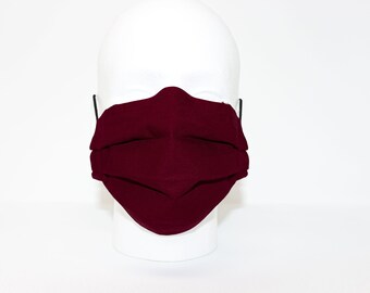 Puede incluir: Una mascarilla facial de color burdeos con pliegues, puesta en una cabeza de maniquí blanca.