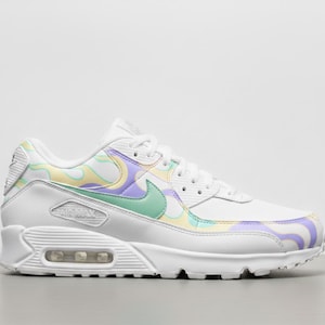 May include: White Air Max 90 trainer with a pastel swirl pattern in yellow, purple, and green. The shoe has a white sole, laces, and a green Nike swoosh logo.