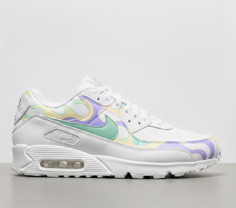 May include: White Air Max 90 trainer with a pastel swirl pattern in yellow, purple, and green. The shoe has a white sole, laces, and a green Nike swoosh logo.