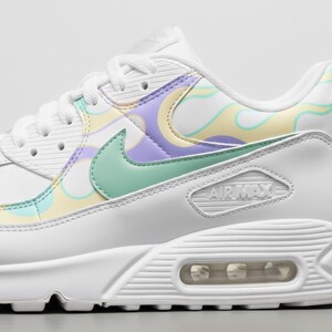 May include: White Air Max 90 trainers with pastel detailing. The shoe has a mint green Nike swoosh and a design of swirling yellow, purple, and light green patterns. The Air Max logo is visible on the side.
