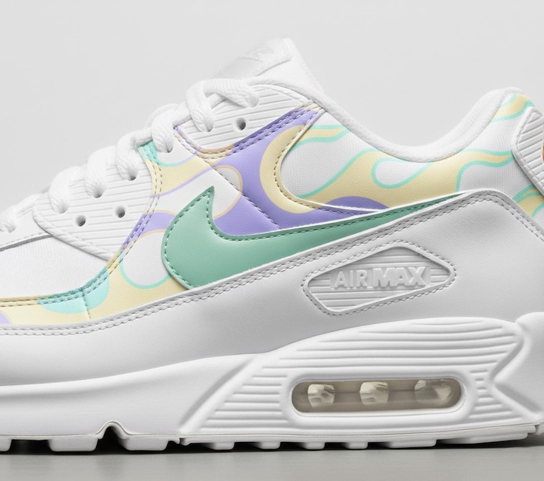 May include: White Air Max 90 trainers with pastel detailing. The shoe has a mint green Nike swoosh and a design of swirling yellow, purple, and light green patterns. The Air Max logo is visible on the side.
