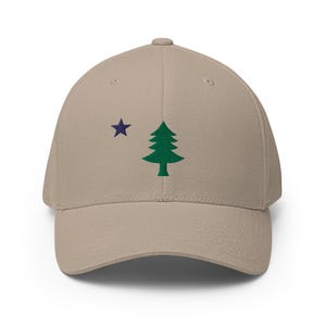 May include: A beige baseball cap with an embroidered green pine tree and a blue star on the front.