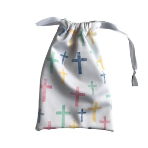 May include: A white drawstring bag with a pattern of colorful crosses in blue, green, yellow, and pink. The bag is tied with a white ribbon. The bag is made of fabric.