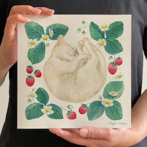 May include: Watercolor painting of a sleeping cream-colored cat surrounded by green strawberry leaves, white flowers, and red strawberries. The artwork is signed "Angela Takagi" in the bottom right corner.