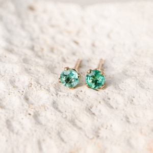 May include: A pair of gold stud earrings with small, round, green gemstones.
