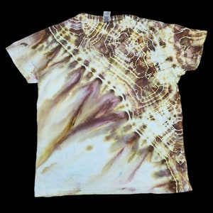 May include: A short-sleeved t-shirt with a tie-dye pattern in shades of brown, white, and purple. The design features a circular pattern on the upper right side and a flowing, organic pattern across the shirt.