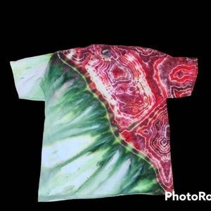 May include: A tie-dye t-shirt with a unique design. The shirt features a blend of colors, including green, red, and white. The design has a marbled effect, with the colors blending together in a swirling pattern. The shirt is made of a soft material.