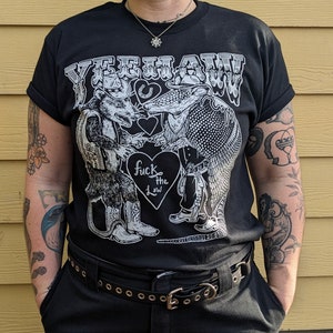 May include: Black t-shirt with a graphic featuring a rat and an armadillo in cowboy attire, the text "YEEHAW!" across the top, and a heart with "fuck the law" in the center. The shirt has rolled-up sleeves.