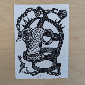 May include: A black and white linocut print depicting a stylized face or mask. The artwork features a cage-like structure with spikes, chains, and a key. The design has a bold, graphic style, with a raw, textured edge.