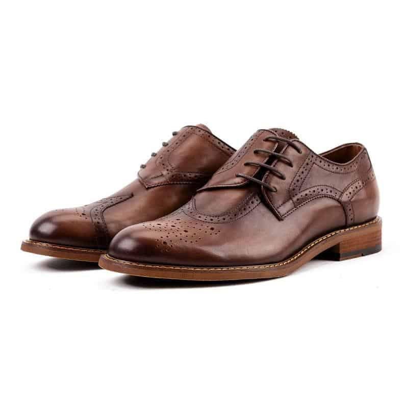 May include: A pair of brown leather lace-up shoes with a wingtip design and a brogue pattern. The shoes have a brown leather sole and a brown leather heel.