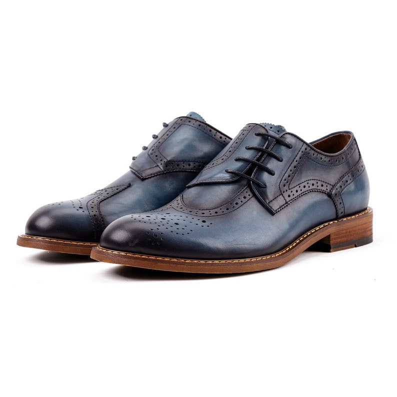 May include: A pair of blue leather lace-up shoes with a brogue design and a brown sole.