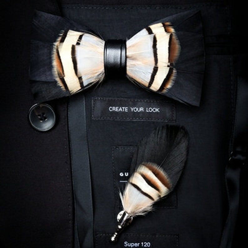 May include: A black and white feather bow tie with a leather accent and a matching black and white feather lapel pin. The text "Create Your Look" is visible on a black label.