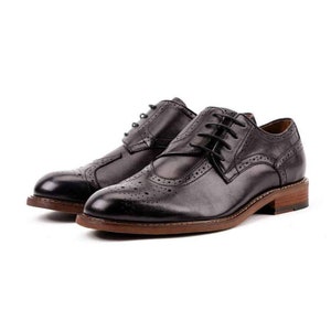 May include: A pair of black leather lace-up shoes with a brogue design. The shoes have a brown leather sole and a rounded toe.
