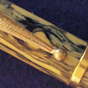 May include: A brown and black marbled pen with a gold band and a gold clip with the inscription "Schreibfeder".