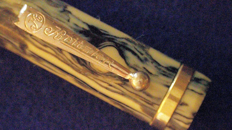 May include: A brown and black marbled pen with a gold band and a gold clip with the inscription "Schreibfeder".